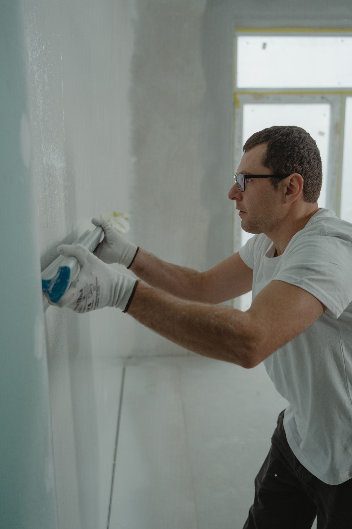 Gloved tradesman applying joint compound to a wall surface with a taping knife